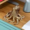 Antique brass octopus desk ornament with textured body and tentacles resting on a wooden surface.
