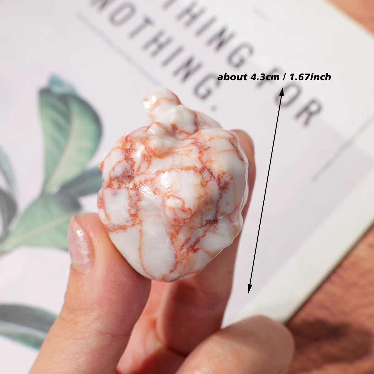 A hand holds a natural crystal heart carving decoration showing white and reddish-orange marbling.
