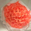 A bouquet of bright orange silk roses wrapped in sheer white tissue paper.
