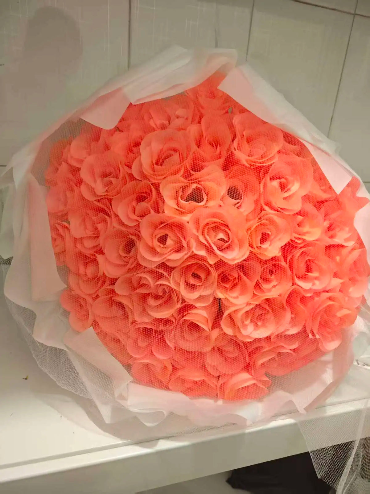 A bouquet of bright orange silk roses wrapped in sheer white tissue paper.