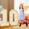 A young girl stands next to large illuminated number balloons spelling '10' in a light marquee frame.
