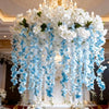 A chandelier adorned with white silk wisteria hanging vine garland flowers.