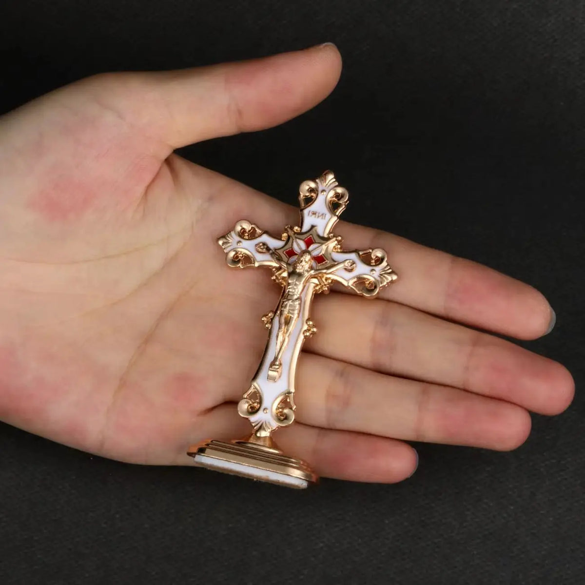 A gold and white metal crucifix desk cross with a self-adhesive base held in a person's hand.