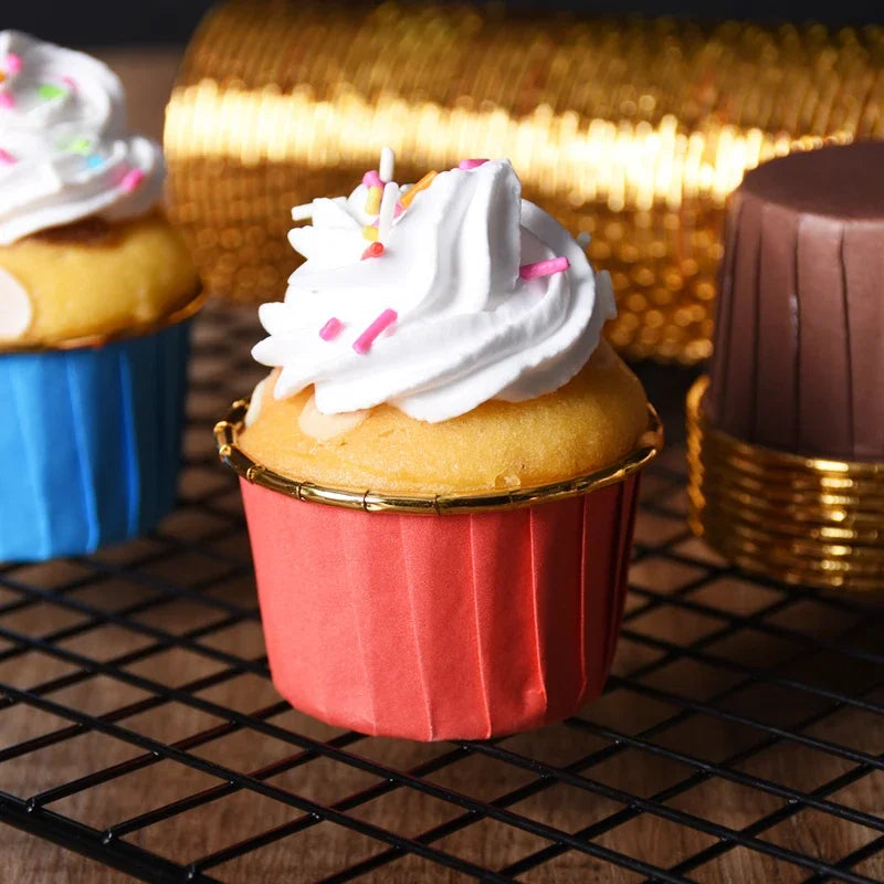 A close-up of a pink cupcake with white frosting on a gold liner, set against a dark wire grid background.