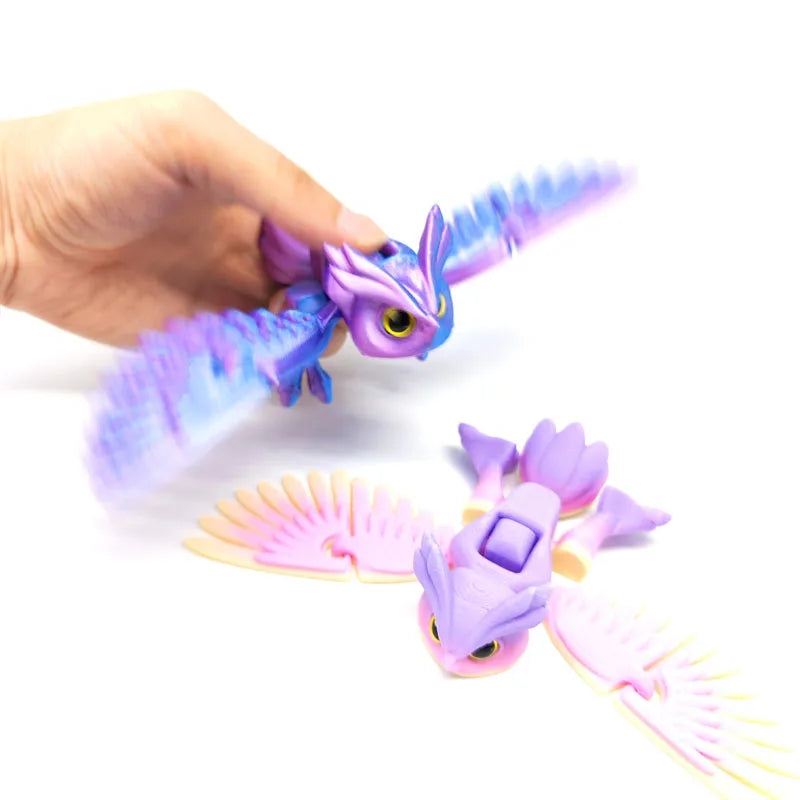 A hand holds a purple articulated 3D printed owl figurine with translucent wings against a white background.