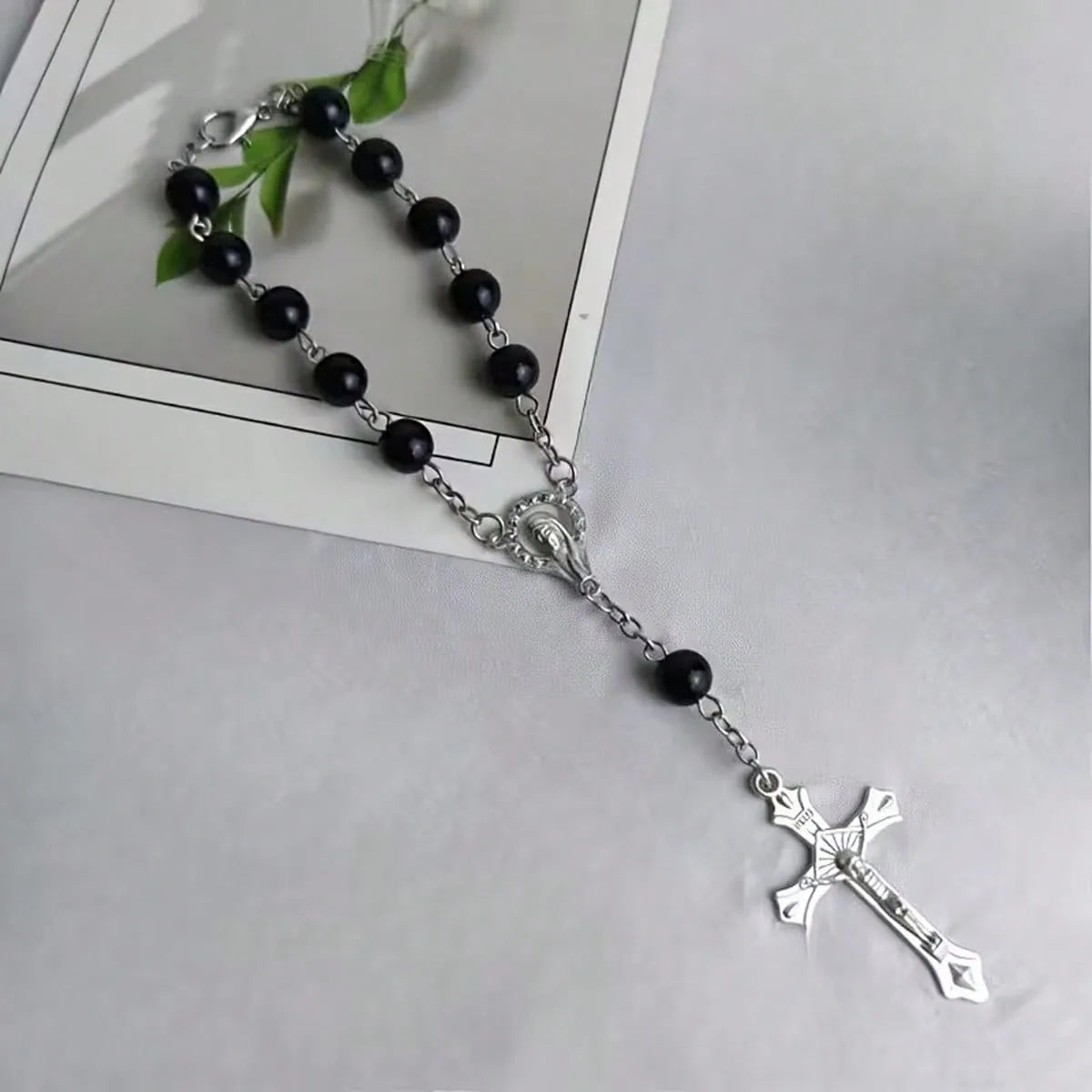 Silver rosary chain with black beads and a cross pendant on a white card.