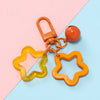 An orange and yellow star charm pendant keychain is displayed on a pink and blue background.