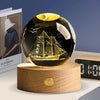 A black crystal ball decoration with a golden interior showing a silhouette of a sailing ship.