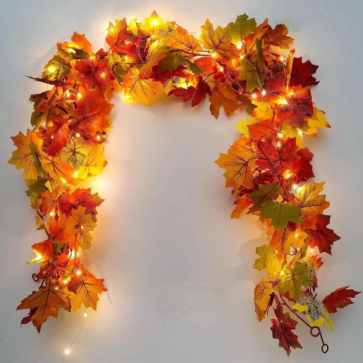 An artificial vine wreath made of autumn maple leaves with warm yellow and orange lights.