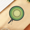 A round foldable hand fan with a green fruit design resting on a light wooden surface.
