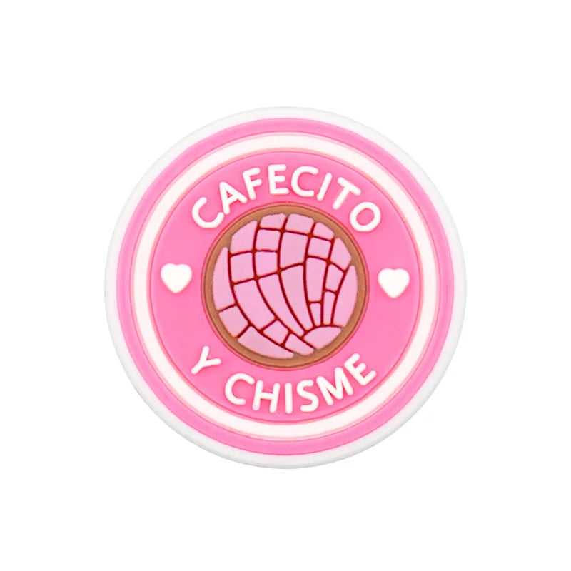 Pink PVC shoe charm with the text cafecito y chisme and a globe design