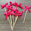 A set of pink satin bows attached to wooden sticks, used as cupcake toppers.