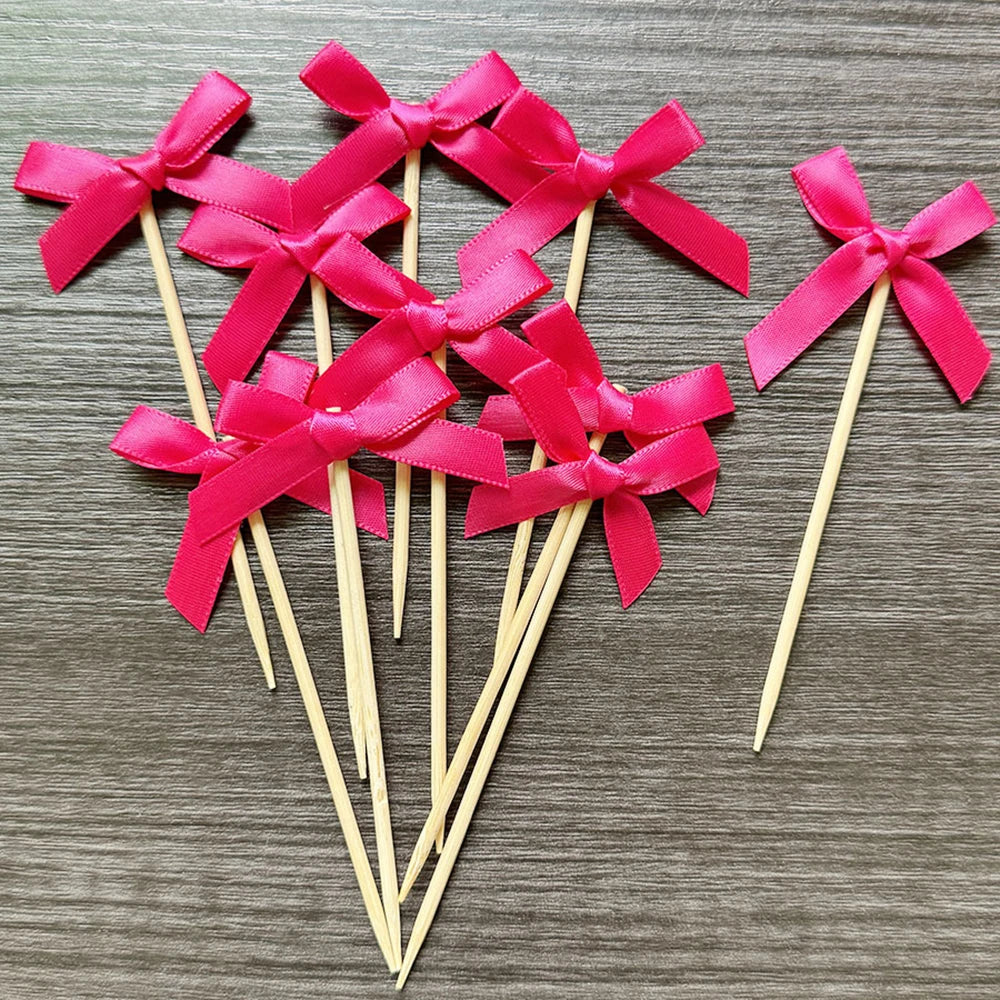 A set of pink satin bows attached to wooden sticks, used as cupcake toppers.