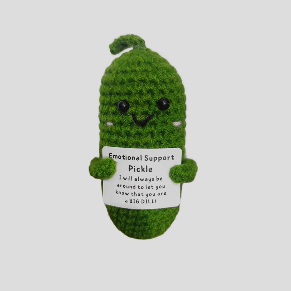 A handmade plush knitting doll shaped like a green pickle with a smiling face and an emotional support message tag.