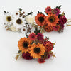 Un bouquet de fleurs artificielles avec des tons orange, blanc et rose foncé/marron.