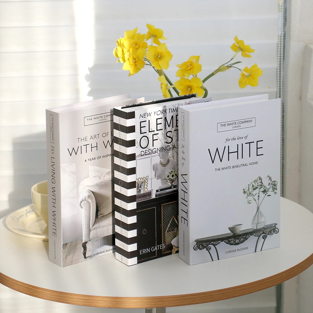 A set of three modern decorative fake books in white with yellow flowers on a light surface.