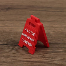 A red wooden sign shaped like an arrow with the text A LITTLE SIGN TO SAY I LOVE YOU engraved on it.