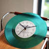 A vintage vinyl record wall clock with a teal cover and brass frame displaying midnight time.