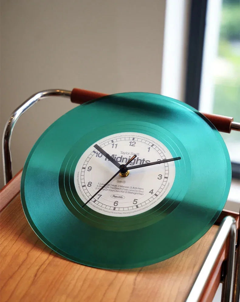 A vintage vinyl record wall clock with a teal cover and brass frame displaying midnight time.
