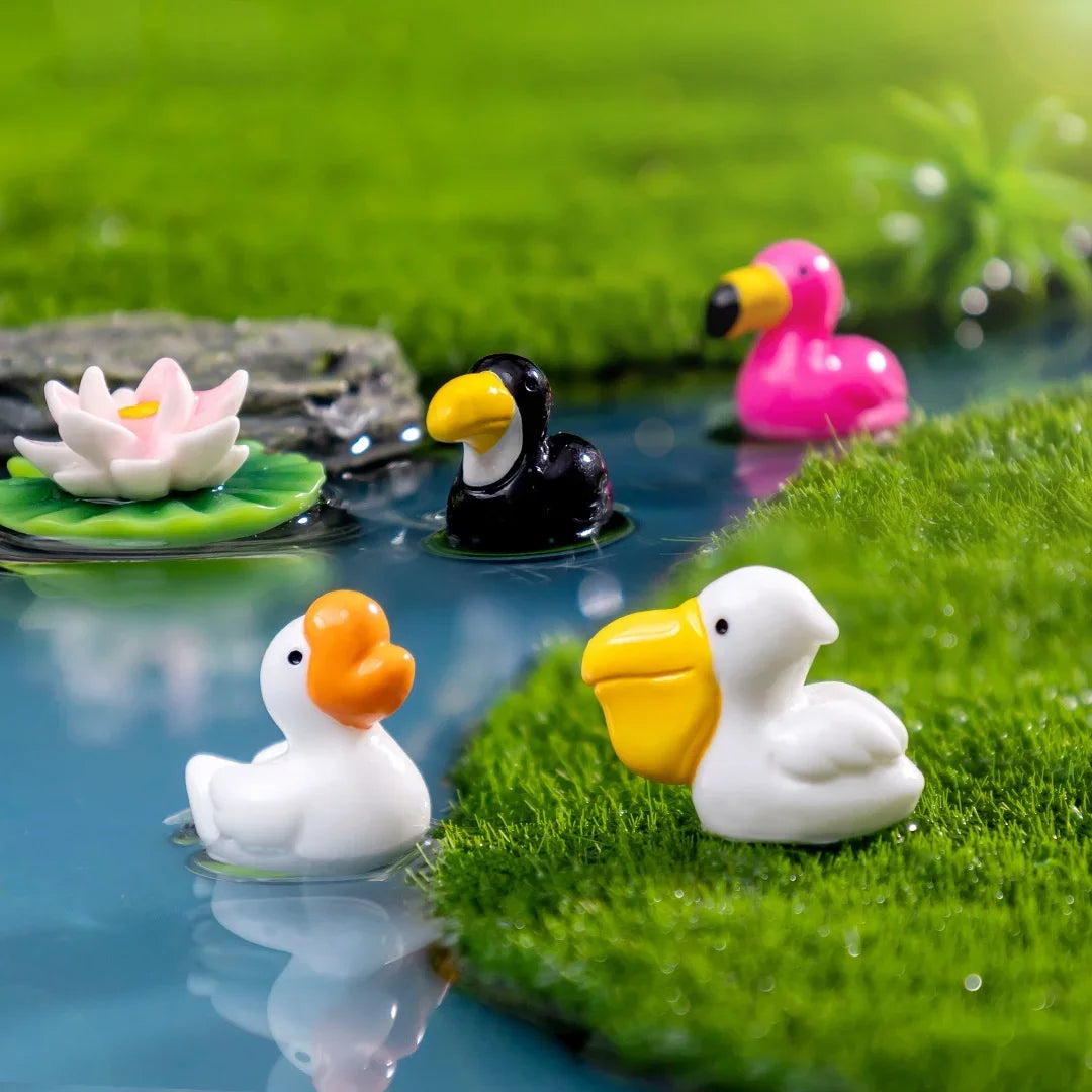Petites sculptures d'animaux en résine : flamant rose et canard blanc sur une surface verte texturée.
