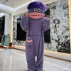 A purple monster onesie pajama suit with large eyes and a pink mouth is displayed indoors.