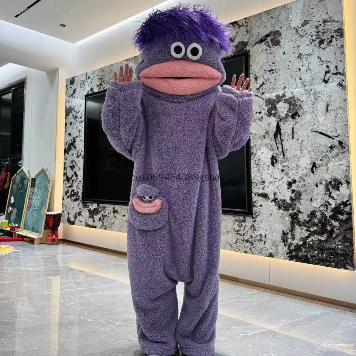 A purple monster onesie pajama suit with large eyes and a pink mouth is displayed indoors.