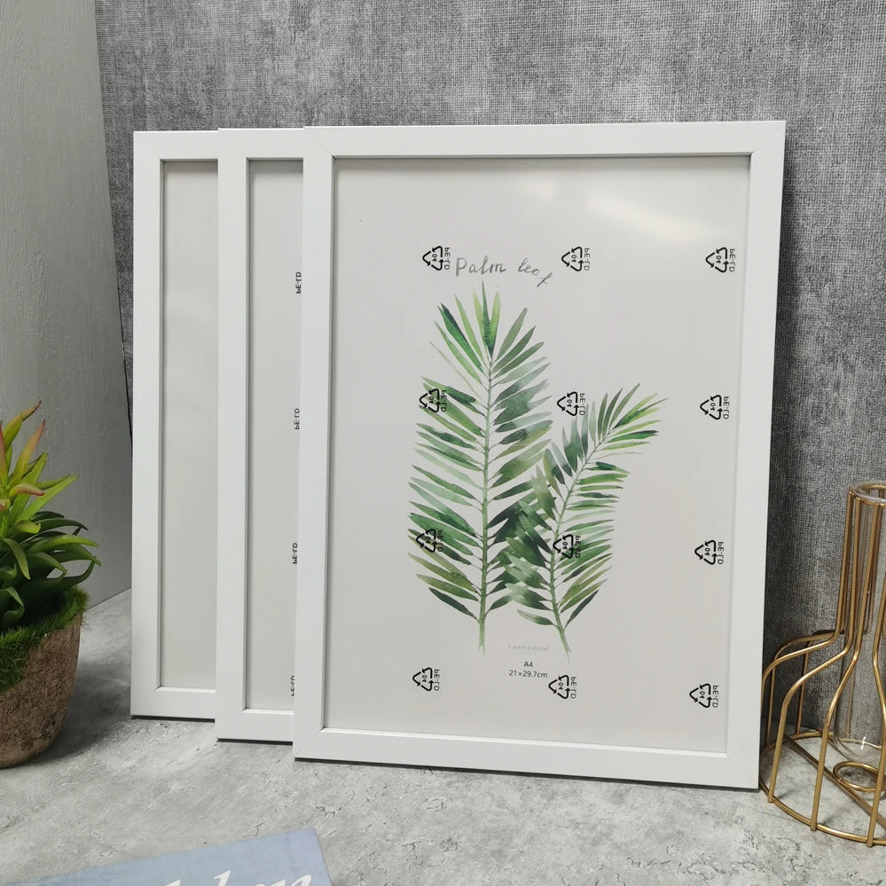 A set of three white wooden photo frames with green palm leaf illustrations for wall decor.