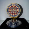 A round brass ornament featuring Latin phrases and symbols on a dark background.
