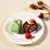 A small chocolate cake decorated with white cream and candied fruit is served on a white paper plate.