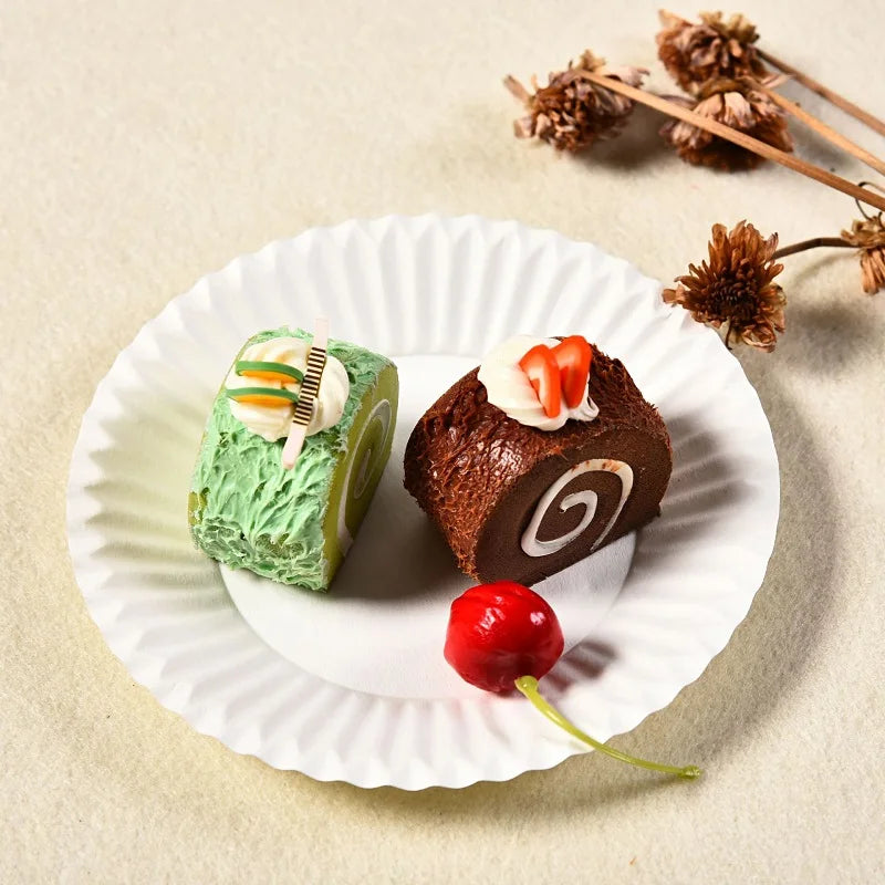 A small chocolate cake decorated with white cream and candied fruit is served on a white paper plate.