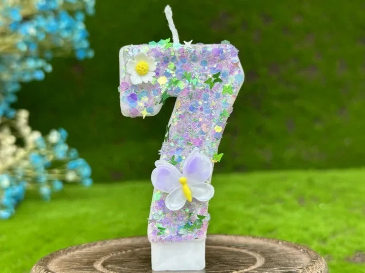A number cake candle shaped like the number 7 decorated with purple glitter, a white flower, and a purple butterfly on a wood