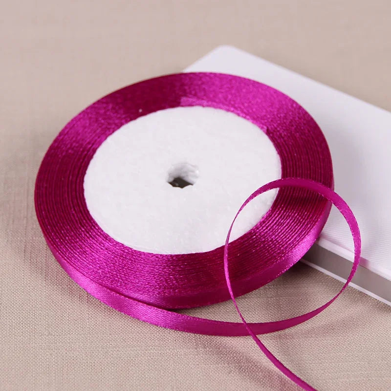 A roll of vibrant magenta satin ribbon on a white spool, ready for gift wrapping or crafts.
