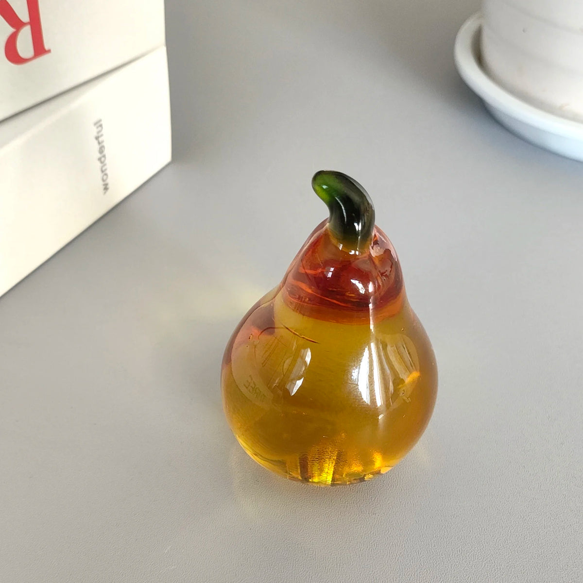 A translucent yellow glass pear figurine with a green stem, resting on a light surface.