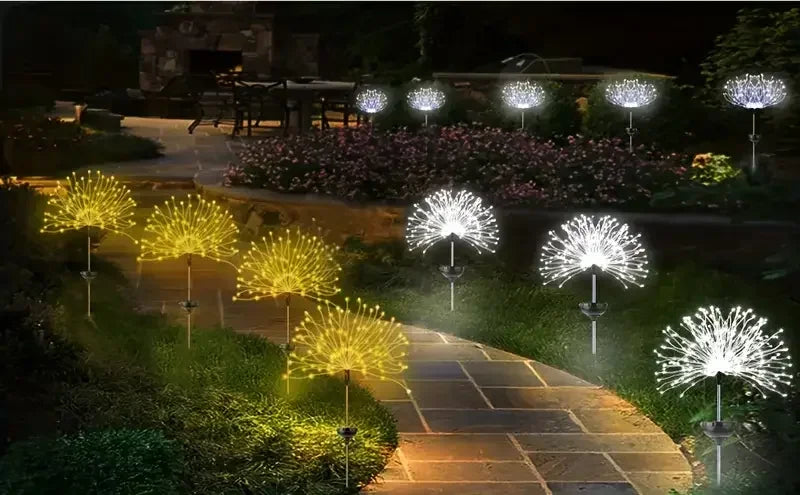 A row of solar fireworks garden lights illuminating a pathway and flower bed at night.