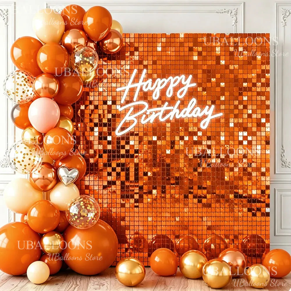 A close-up of a square gold sequin wall backdrop decorated with round orange and gold balloons and the text Happy Birthday