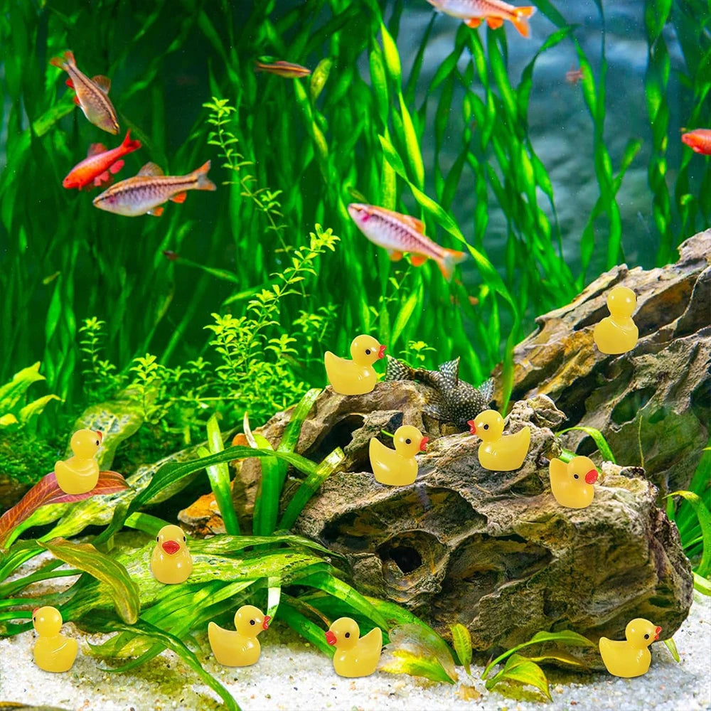 A collection of yellow resin duck figurines resting on green aquatic plants and rocks.