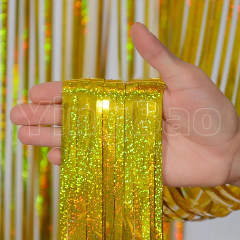 A hand holds a vertical strand of bright yellow metallic foil tinsel fringe against a shimmering gold and white backdrop.