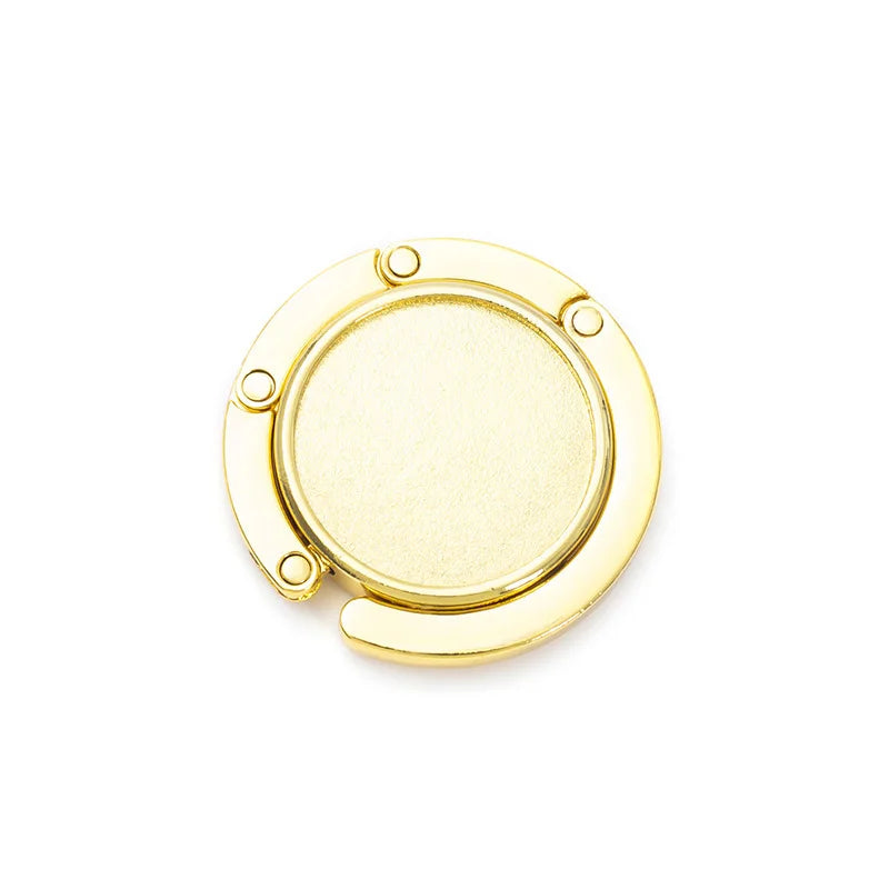 A round, gold-colored compact folding table bag hook or portable purse hanger.