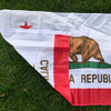 A white and red flag featuring a brown bear silhouette and text on a green background, laid out on green grass.