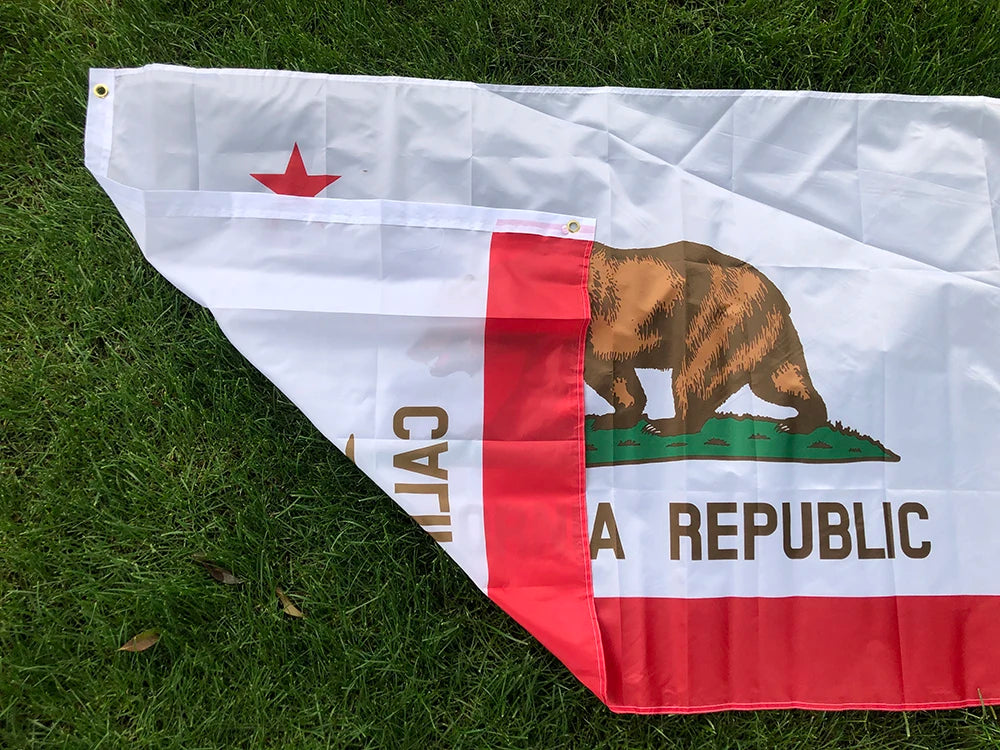 A white and red flag featuring a brown bear silhouette and text on a green background, laid out on green grass.