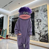 A purple monster onesie pajama suit with large eyes and a pink mouth stands in a brightly lit room.