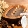 A wooden bowl filled with sand and several lit candles, surrounded by pine cones and dried grasses.