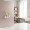 A small glass flower vase with a yellow flower is magnetically attached to a pink wall.
