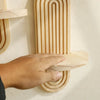 A hand is placing a wooden arc wall shelf onto a textured white wall.