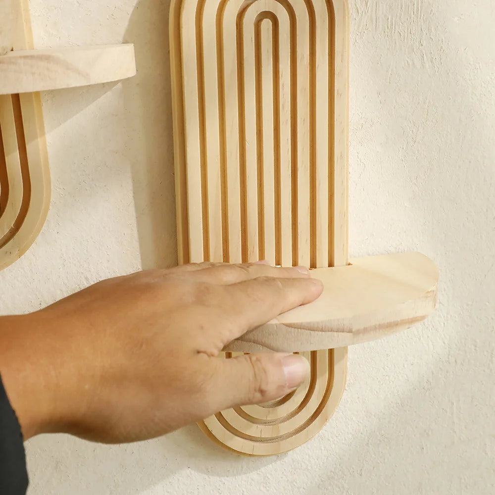 A hand is placing a wooden arc wall shelf onto a textured white wall.