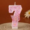 A pink glitter candle shaped like the number 7 with a butterfly decoration.