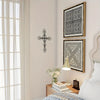 A framed metal cross and geometric pattern wall decor displayed on a light-colored wall next to a window.
