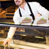 A man in a white shirt and apron is preparing or handling clear triangle cake slice containers filled with cake.