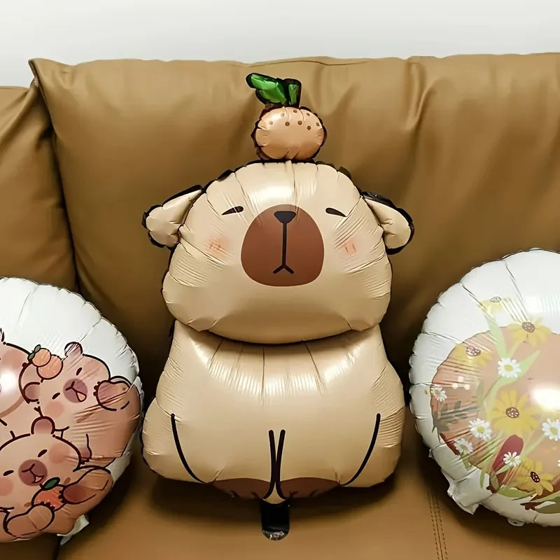 A brown foil balloon shaped like a capybara is displayed on a tan couch with other animal-themed balloons.