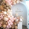 A large arrangement of assorted pink and beige latex balloons forming an archway backdrop for a baby celebration.